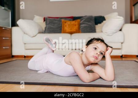 S'ennuient une petite fille pensive en léopard couchée sur le sol regarder loin tout en se reposant pendant la répétition de ballet à la maison Banque D'Images