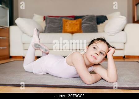 S'ennuient une petite fille pensive en léopard couchée sur le sol regarder loin tout en se reposant pendant la répétition de ballet à la maison Banque D'Images