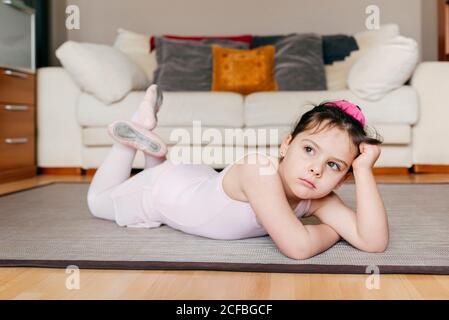 S'ennuient une petite fille pensive en léopard couchée sur le sol regarder loin tout en se reposant pendant la répétition de ballet à la maison Banque D'Images