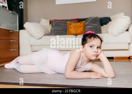 S'ennuient une petite fille pensive en léopard couchée sur le sol regarder loin tout en se reposant pendant la répétition de ballet à la maison Banque D'Images