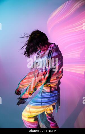 Vue latérale d'une jeune femme dans une tenue tendance dansant sous un éclairage coloré Banque D'Images