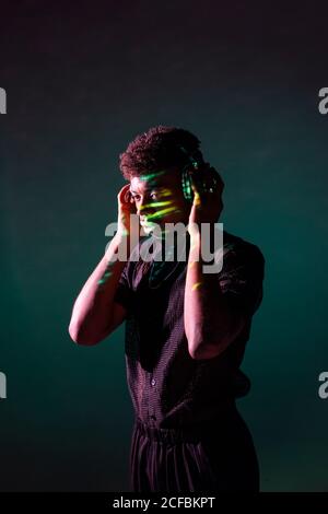 Un jeune homme afro-américain séduisant dans un casque qui écoute de la musique sur fond vert foncé Banque D'Images