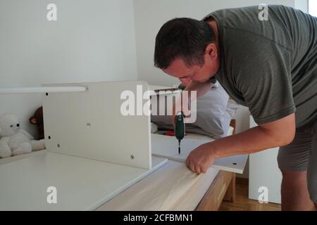 Homme assemblant des meubles avec un tournevis électrique sans fil. Il améliore sa maison avec un nouveau bureau d'ordinateur. Le kit DIY a été commandé sur un magasin en ligne. Banque D'Images