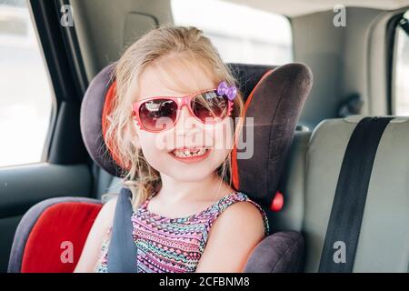 Jeune fille portant des lunettes de soleil assis dans un siège d'auto Banque D'Images