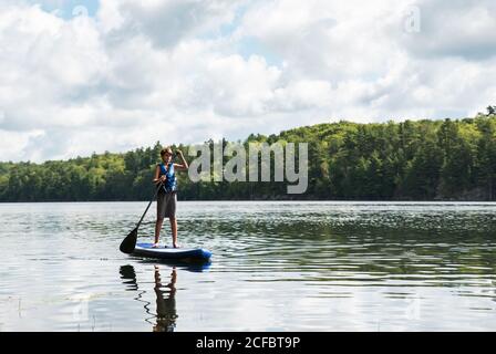 Un jeune garçon pagayant sur un SUP sur le lac en Ontario, au Canada, par une journée ensoleillée. Banque D'Images