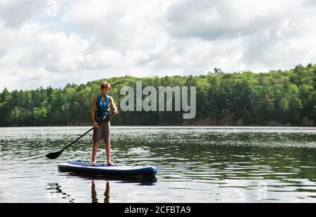 Un jeune garçon pagayant sur un SUP sur le lac en Ontario, au Canada, par une journée ensoleillée. Banque D'Images