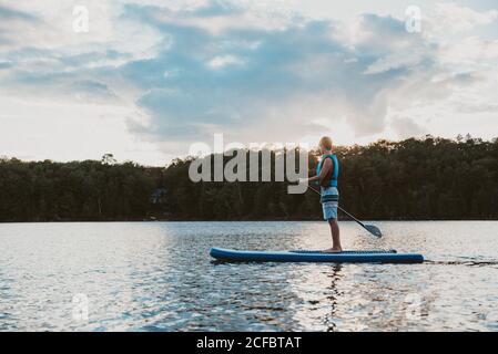 Un jeune garçon pagayant sur un SUP sur le lac en Ontario, au Canada, par une journée ensoleillée. Banque D'Images