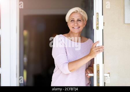 Femme souriante debout à la porte de sa maison Banque D'Images
