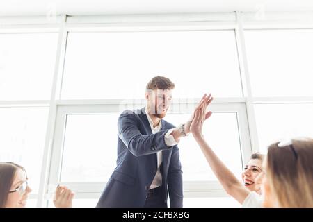 Camarades de classe femmes et hommes célébrant l'examen de mathématiques de la pathing, se sentant excitant et gai , donnant élevé cinq pendant la réunion informelle en amical Banque D'Images