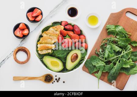 Vue de dessus du poulet frit et des fraises placées près de l'avocat les moitiés sur les épinards partent sur la table en marbre près des ustensiles et sauces aux épices Banque D'Images