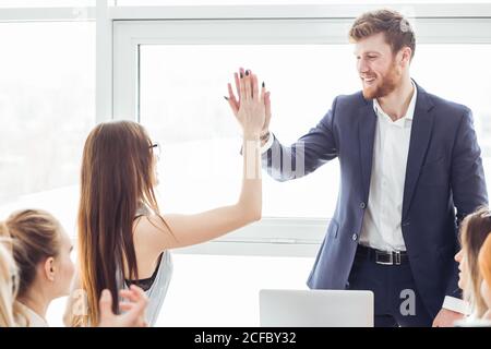 Camarades de classe femmes et hommes célébrant l'examen de mathématiques de la pathing, se sentant excitant et gai , donnant élevé cinq pendant la réunion informelle en amical Banque D'Images