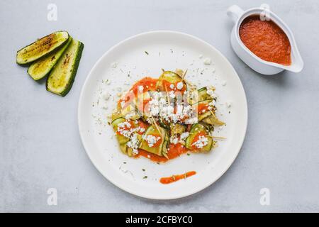 Vue de dessus de l'assiette ronde blanche avec salade de frits concombre avec fromage de chèvre et sauce tomate sur une surface grise Banque D'Images