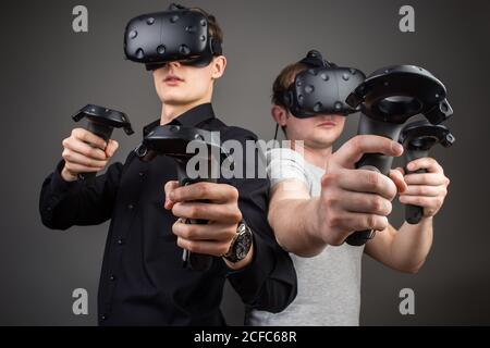 Photo de deux jeunes homme debout avec des lunettes de VR et de garder une manette de jeu ou un doigt comme une arme Banque D'Images