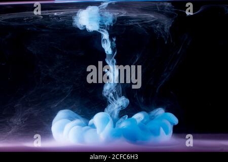 la peinture bleue coule dans l'eau sur fond sombre. Banque D'Images