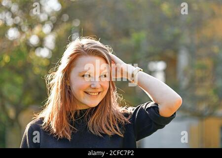 Jeune fille avec cheveux rougeâtre et freckles est à l'extérieur et sourit au portrait de l'appareil photo Banque D'Images