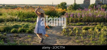 enfance, provence style concept - bannière 3 ans blonde petite fille enfant en robe bleue et chapeau de paille aspect slave courir le long du chemin avec le jouet Banque D'Images