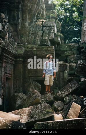 Homme de voyage avec sac à dos debout sur une pile de blocs de pierre de mousse explorant l'ancien temple en ruines, Thaïlande Banque D'Images