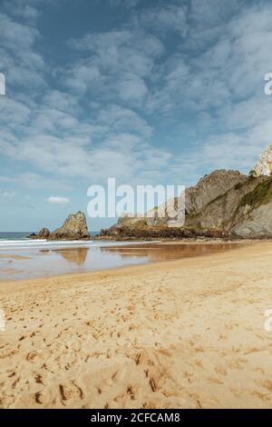 Vue magnifique sur l'océan paisible et la plage de sable avec empreintes de pieds près du grand rocher dans l'après-midi sous le ciel bleu avec des nuages Banque D'Images