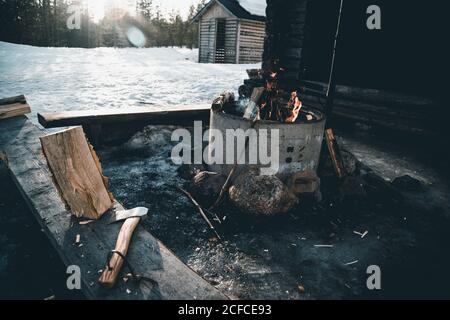 Feu de camp et feu de bois avec hache placé près de la petite cabine de bûcherons dans la forêt enneigée en hiver dans la campagne De Finlande Banque D'Images
