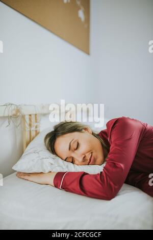Jeune jolie femme en pyjama souriant en dormant sur le lit dans la chambre Banque D'Images