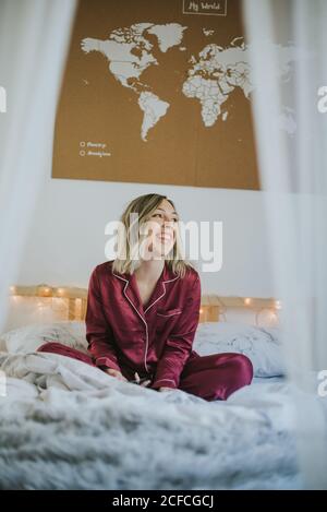 Jeune femme en pyjama assis sur le lit donnant sur l'extérieur Banque D'Images