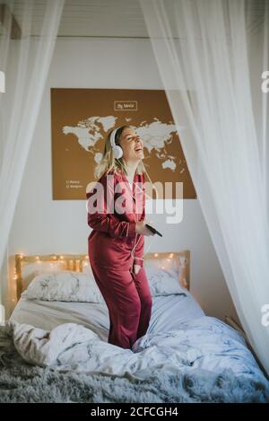 Jeune femme souriante en pyjama avec casque dansant au lit le matin Banque D'Images