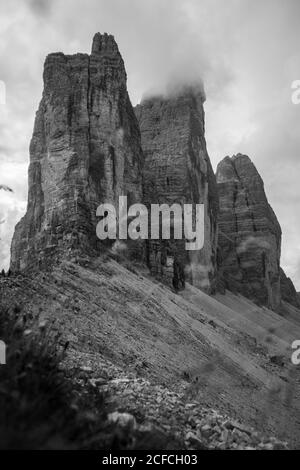 vue en noir et blanc depuis les contreforts avec herbe verte et Petites roches de pics brumeux des montagnes Drei Zinnen in Dolomites par temps couvert Banque D'Images