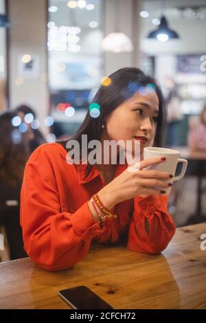Tout au long d'un verre vue de la jeune femme ayant une tasse de café à table dans le café Banque D'Images