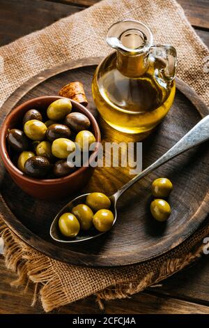 Du dessus du bol en verre avec de l'huile vierge supplémentaire assiette en bois avec olives noires et vertes Banque D'Images