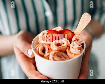 Glace roulée avec fraise dans une tasse conique dans les mains de femme. Porte-gobelet conique avec glace en rouleau de style thaïlandais Banque D'Images
