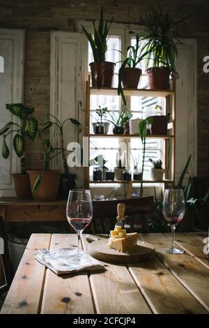 Verres avec vin rouge placés près du fromage sur une table en bois dans un restaurant rustique avec plantes vertes en pot sur la fenêtre Banque D'Images