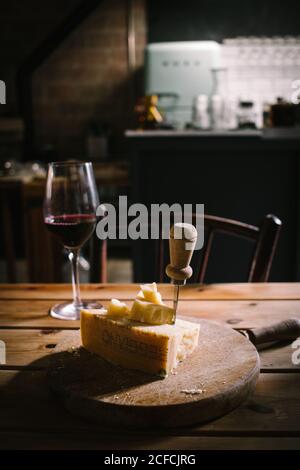 Morceau de délicieux fromage avec couteau servi sur une planche de bois placé près d'un verre de vin rouge sur une table en bois dans le bar rustique Banque D'Images