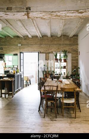 Grande table et chaises en bois dans un bar rustique de style rétro avec plafond en sorbrée et plantes vertes en pot sur la fenêtre Banque D'Images