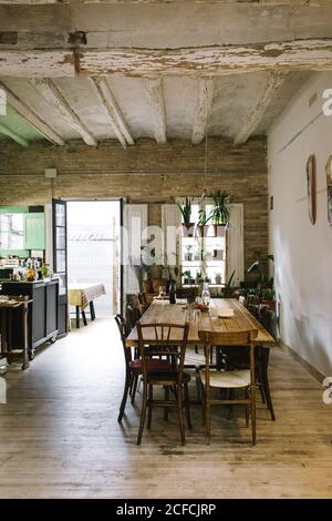 Grande table et chaises en bois dans un bar rustique de style rétro avec plafond en sorbrée et plantes vertes en pot sur la fenêtre Banque D'Images