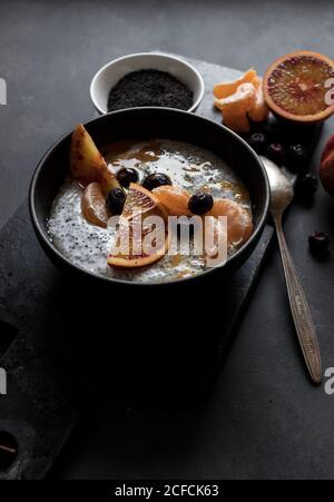 De dessus chia graines pudding avec des tranches d'orange, mandarines et olives dans un bol près de la cuillère et pamplemousse sur table sombre Banque D'Images