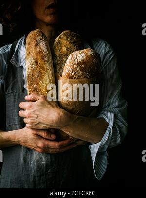 Femme coupée en tablier tenant du pain de ciabatta tout en se tenant debout sur un arrière-plan sombre Banque D'Images
