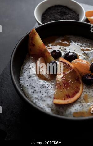 De dessus chia graines pudding avec des tranches d'orange, mandarines et olives dans un bol près de la cuillère et pamplemousse sur table sombre Banque D'Images