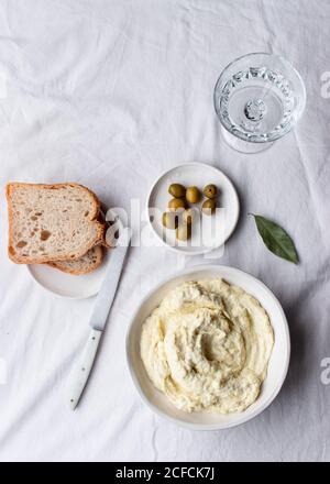 De dessus bol avec codfish brandade placé près des olives, des tranches de pain et des feuilles de baie sur une table de cuisine fond blanc Banque D'Images