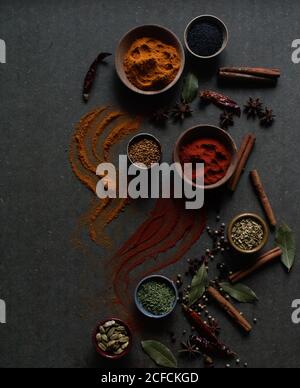 Composition vue de dessus avec différents types d'épices aromatiques naturelles placé sur fond gris foncé avec une épice en poudre déversée la surface Banque D'Images