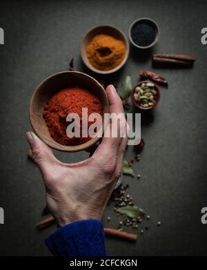 Vue de dessus de la récolte personne non reconnaissable tenant le pot avec le rouge paprika poudre sur table grise avec ensemble d'aromatiques assortis épices Banque D'Images