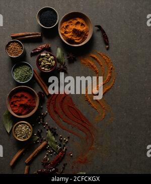 Composition vue de dessus avec différents types d'épices aromatiques naturelles placé sur fond gris foncé avec une épice en poudre déversée la surface Banque D'Images