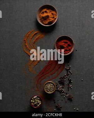 Composition vue de dessus avec différents types d'épices aromatiques naturelles placé sur fond gris foncé avec une épice en poudre déversée la surface Banque D'Images