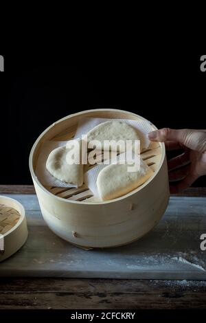 Crop person Cook tenant le cuiseur vapeur de bambou avec la feuille de lotus brute Petits pains pour Gua Bao à la table Banque D'Images