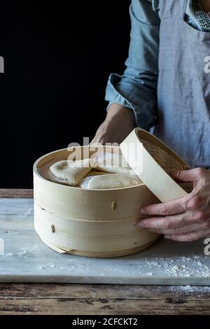 Crop person Cook tenant le cuiseur vapeur de bambou avec la feuille de lotus brute Petits pains pour Gua Bao à la table Banque D'Images