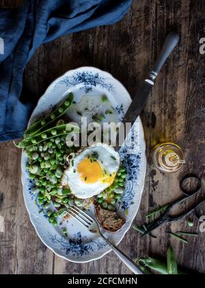 Du dessus de l'assiette avec pain grillé et sauté pois verts et œuf frit sur une table en bois Banque D'Images