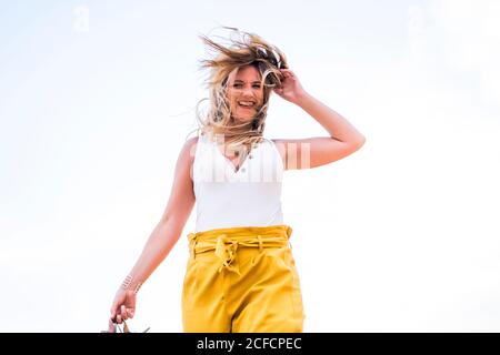 Joyeuse femme blonde élégante tenant des chaussures en marchant dans le désert du Maroc Banque D'Images