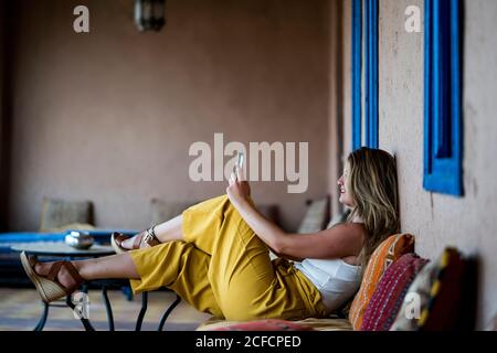 Femme adulte assise sur un canapé en terrasse de style oriental et utilisant un téléphone portable au Maroc Banque D'Images