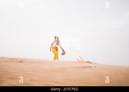 Joyeuse femme blonde élégante tenant des chaussures en marchant dans le désert du Maroc Banque D'Images