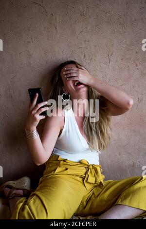 Bonne femme blonde assise sur un canapé en terrasse de style oriental et utilisant un téléphone portable au Maroc Banque D'Images