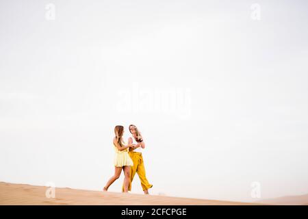 Joyeux et élégant deux femmes blondes amis utilisant le téléphone portable pendant Marche dans le désert du Maroc Banque D'Images